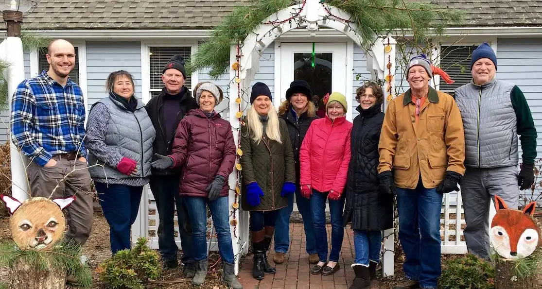 Group of people standing together outside a house in winter clothing.